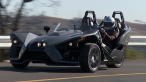 A black Polaris Slingshot drives down a highway.