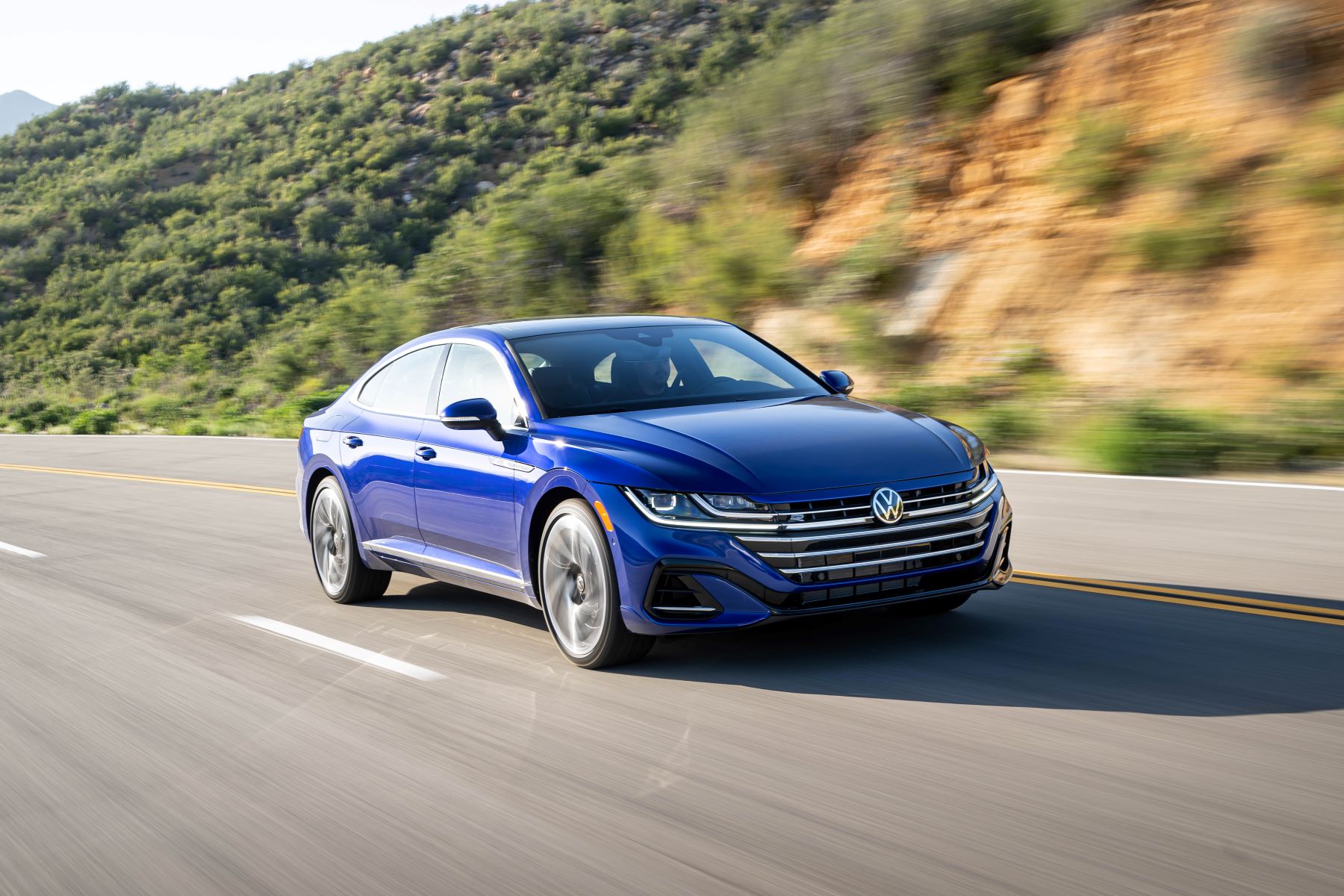 A blue 2022 Volkswagen Arteon fastback sedan model driving on a country highway near forest hills