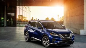 A blue 2023 Nissan Murano midsize crossover SUV parked outside a glass panel office building as the sun sets
