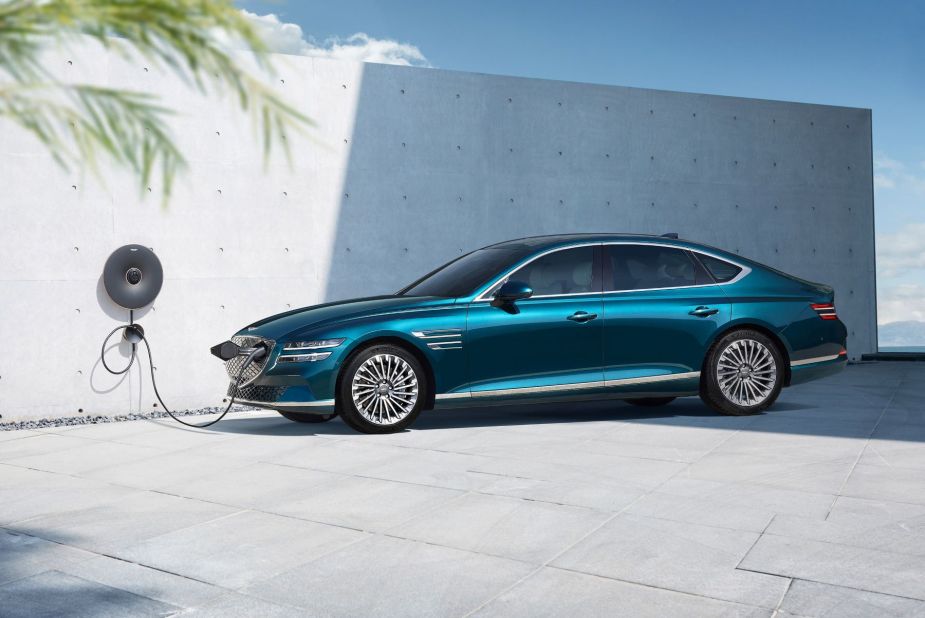 A teal Genesis Electrified G80 midsize EV sedan model plugged into a charging station