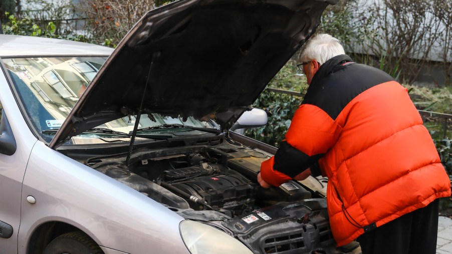 A person looking under the hood, potentially going to administer an engine cleaner.