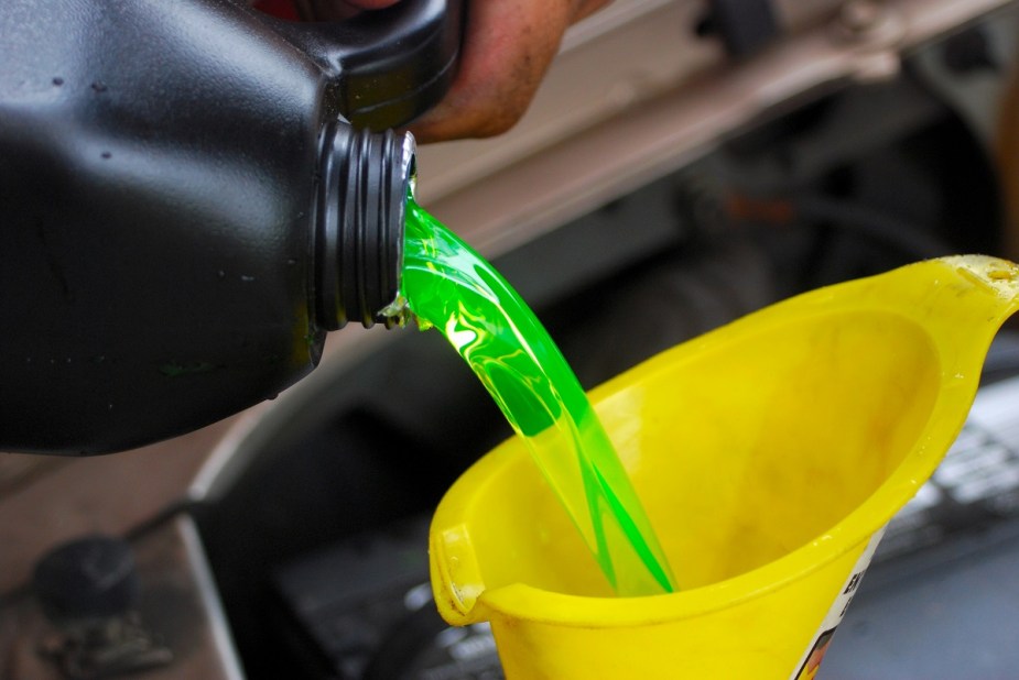 A jug of coolant is being poured into a yellow funnel under an open car hood.