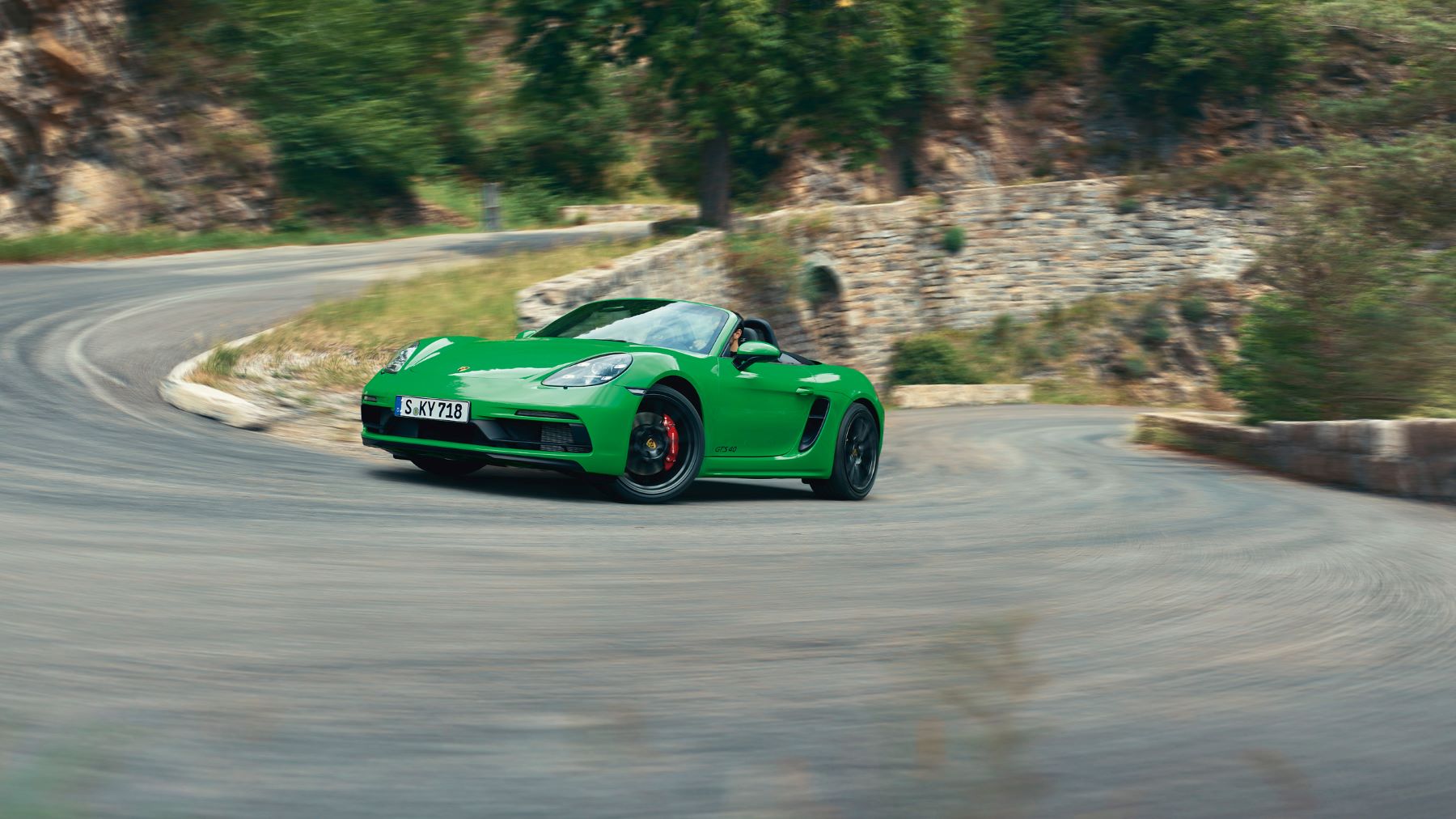 A green Porsche 718 Boxster GTS performance coupe sports car model driving around a twisting country highway