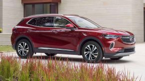 A red 2023 Buick Envision premium midsize SUV model parked on the driveway of a luxury home