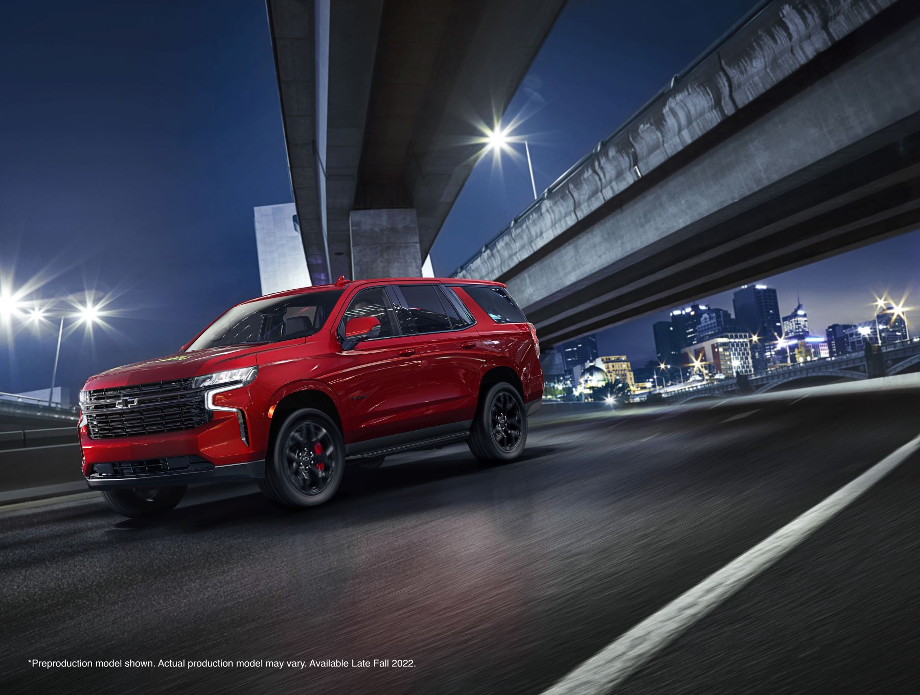 A red 2023 Chevy Tahoe RST Performance Edition full-size SUV driving under a highway overpass at night
