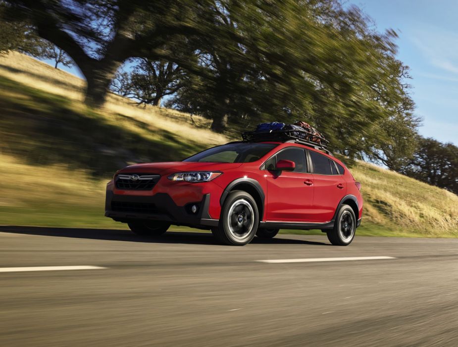 A red 2023 Subaru Crosstrek Premium compact SUV model with a roof rack driving down a highway