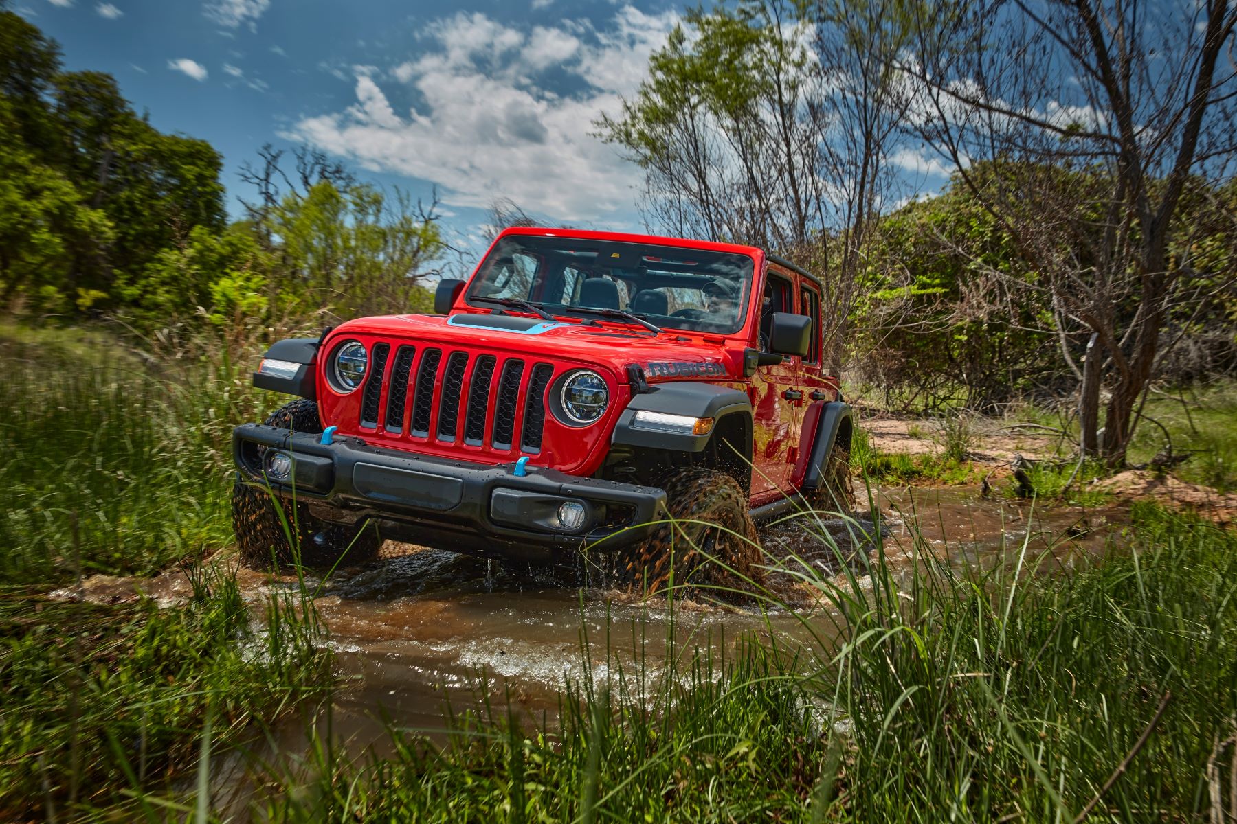 A red model 2023 Jeep Wrangler 4xe plug-in hybrid (PHEV) driving through a swamp