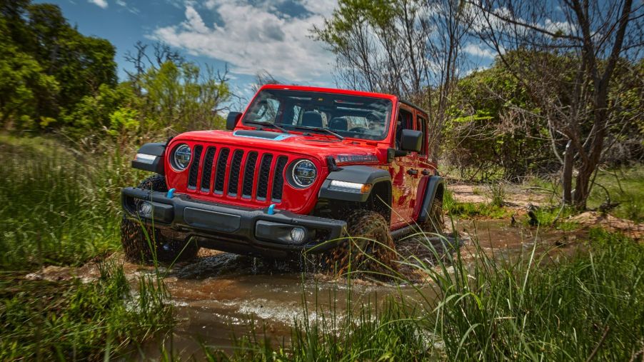 A red 2023 Jeep Wrangler 4xe plug-in hybrid (PHEV) model driving through a swamp