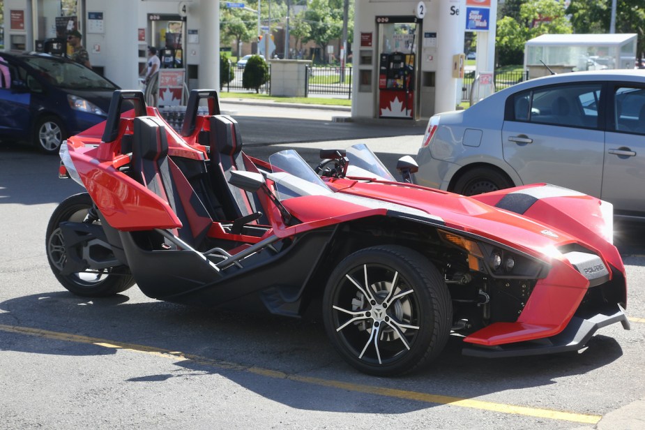 A red Polaris Slingshot parked at a gas station.