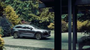 A steel gray Mazda CX-9 midsize SUV model parked outside of an excluded forest home