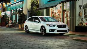 A white 2022 Subaru Impreza compact sedan parked on a downtown tiled street at night near open shops