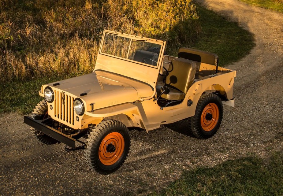 Tan Willys Jeep CJ-2A parked on a dirt road beneath a setting sun.