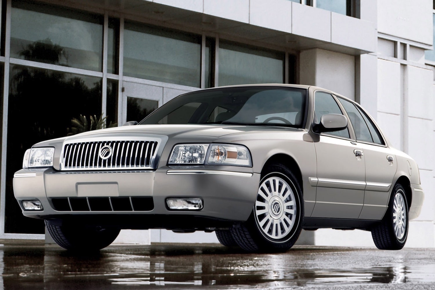 Promo photo of a gray 2007 Mercury Grand Marquis which is a reliable used luxury sedan car that you can buy for under $10k, a building visible in the background.