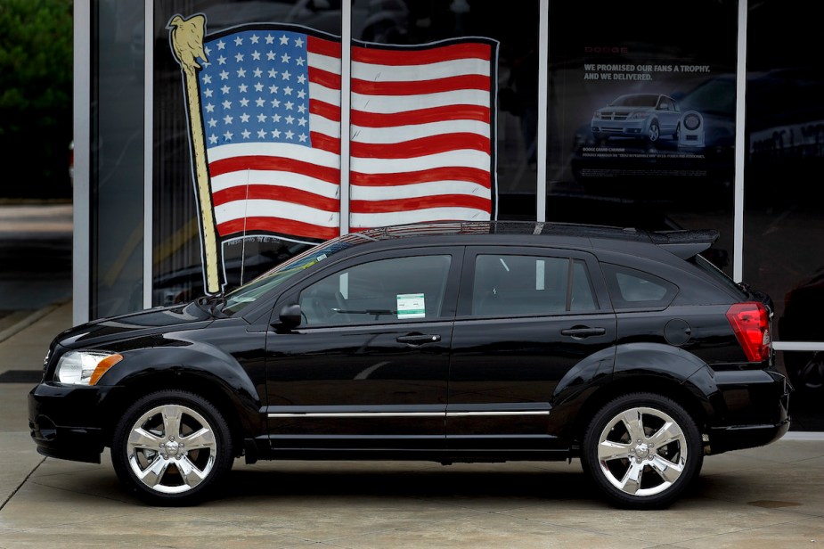 A black 2010 Dodge Journey parked in front of the window with an American flag in the window.