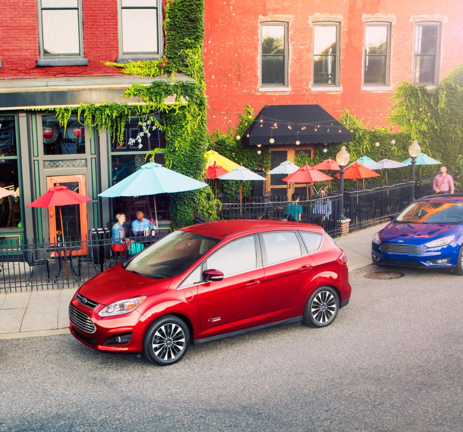 Red used plug-in hybrid crossover SUV by Ford parked on the street, a cafe visible in the background.