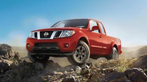 Promo photo of a red Nissan Frontier 4x4 reliable midsize pickup truck parked atop a rock pile, a cloudless blue sky visible in the background.