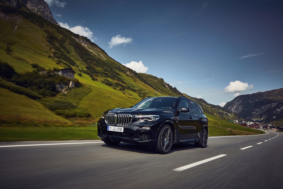 Black BMW X5 plug-in hybrid SUV driving up a winding mountain road, a village visible in the background.