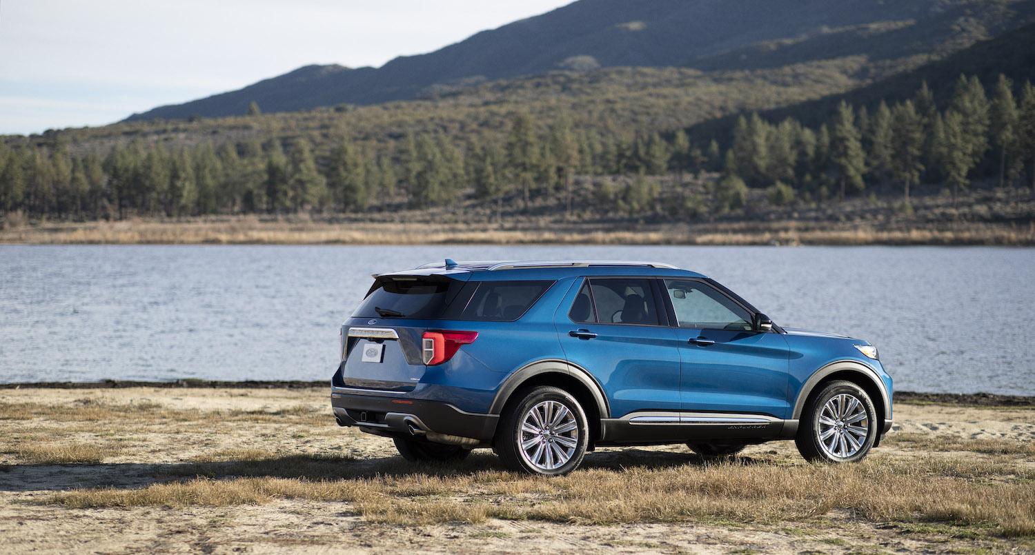 Promo photo of a blue Ford Explorer hybrid SUV parked by a lake, mountains visible in the background.