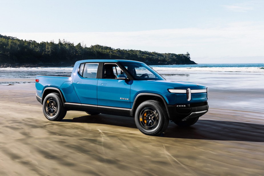 Promo photo of a blue Rivian R1T electric truck driving along a beach.