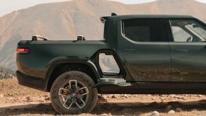 A Rivian electric truck parked in the desert with both its gear tunnel doors open so you can see all the way through the pickup, mountains visible in the background.