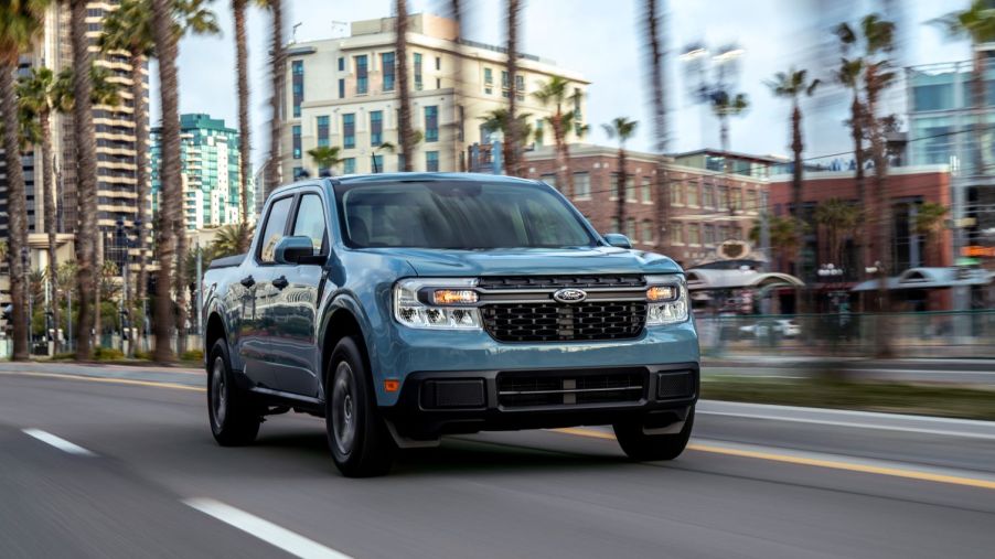 A blue-gray 2022 Ford Maverick Hybrid XLT compact pickup truck driving past palm trees