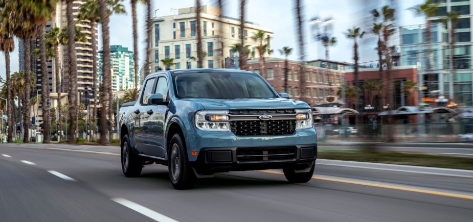 A teal gray 2022 Ford Maverick Hybrid XLT compact pickup truck driving past palm trees