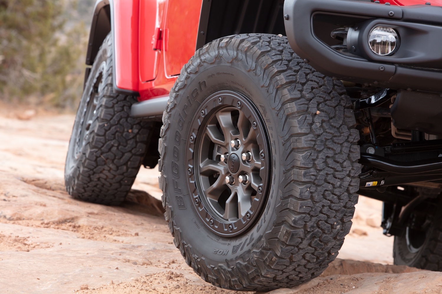Closeup of a red Jeep Wrangler hybrid SUV with oversized tires navigating a 4x4 trail.