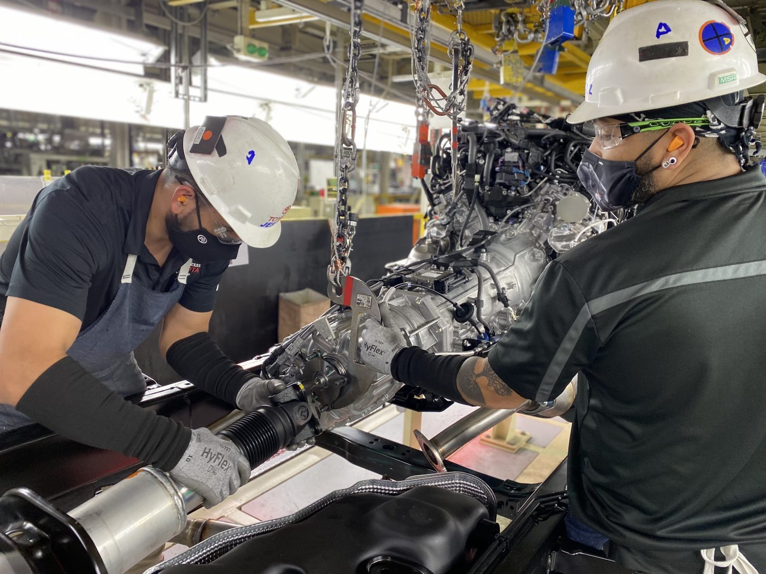 Factory workers assembling the 2022 Toyota Tundra's i-force max hybrid engine with its nickel metal hydride battery pack in a Texas plant.