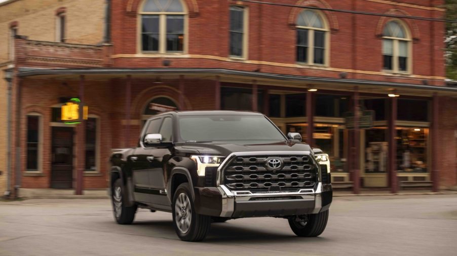 Promo photo of a brown Toyota Tundra hybrid pickup truck driving in front of a brick building using its nickel metal hydrid battery pack.