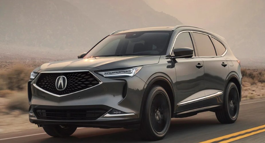 A gray 2023 Acura MDX midsize SUV is driving on the road.