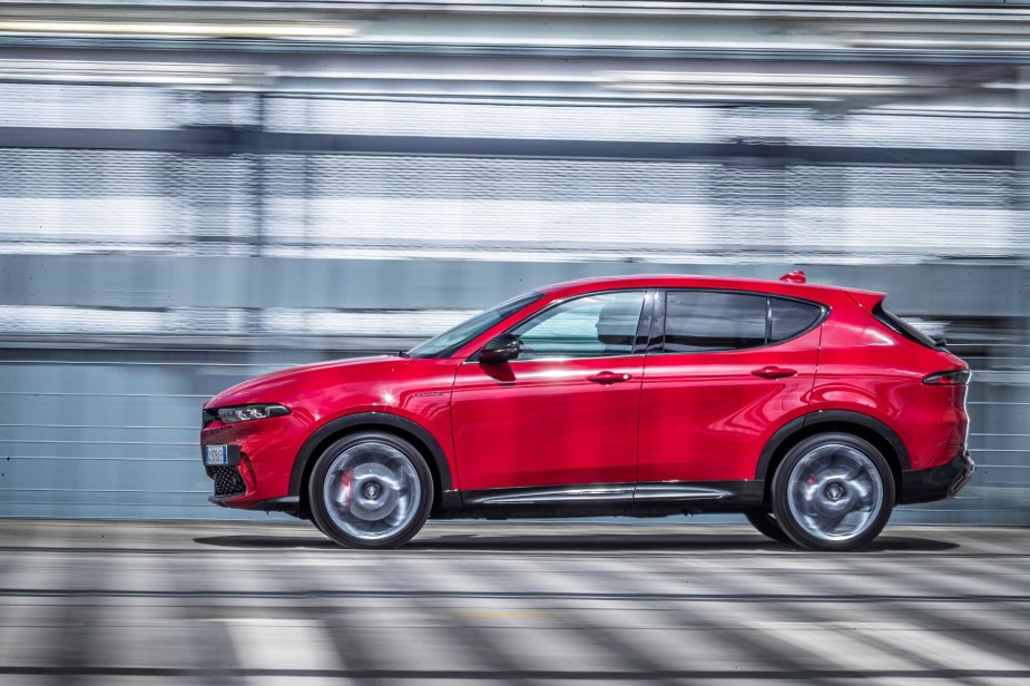 A side profile shot of a red 2023 Alfa Romeo Tonale plug-in hybrid electric vehicle (PHEV) SUV model with a blurred background