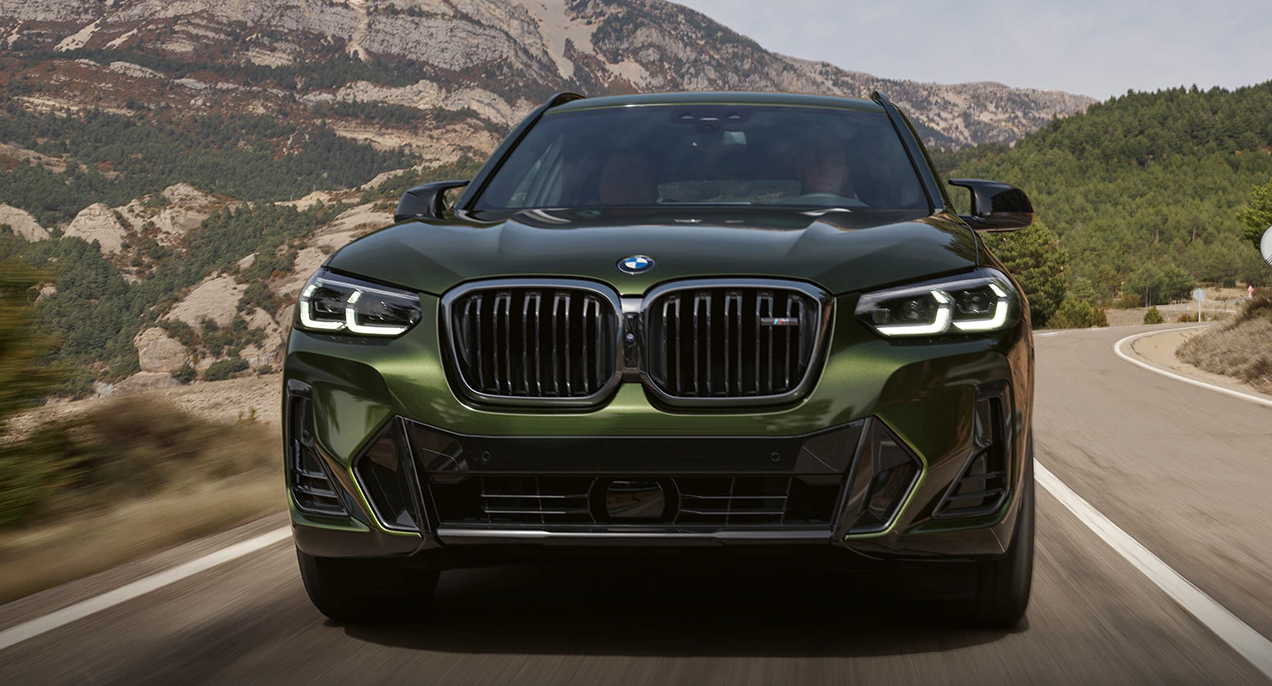 A green 2023 BMW X3 small luxury SUV is driving on the road.