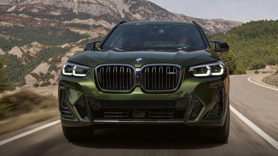 A green 2023 BMW X3 small luxury SUV is driving on the road.