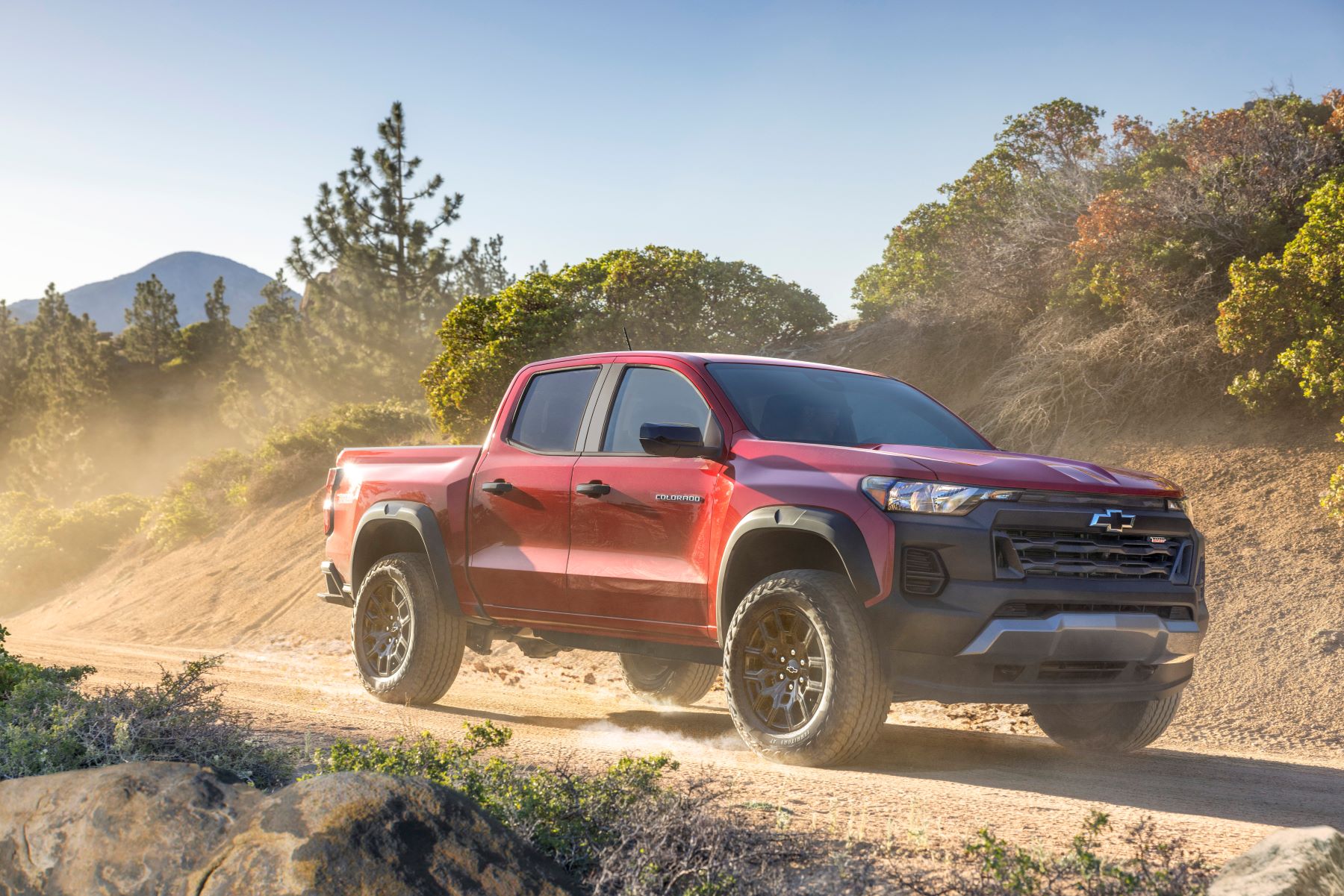 A red 2023 Chevy Colorado Trail Boss midsize pickup truck model parked on a dusty dirt trail in the desert