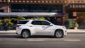 A side profile shot of a white 2023 Chevy Traverse full-size crossover SUV model driving through a city