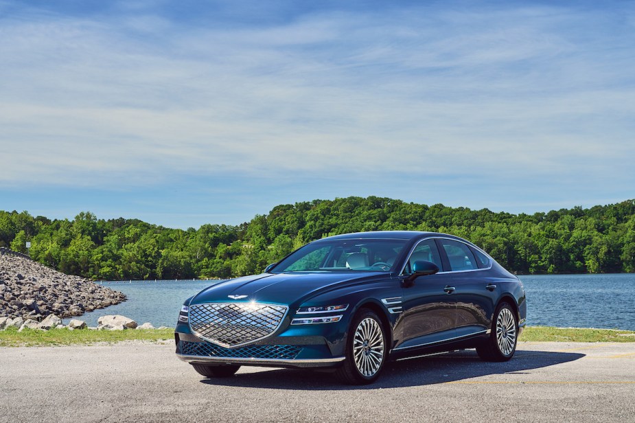 A blue 2023 Electrified Genesis GV80 parked in front of body of water.