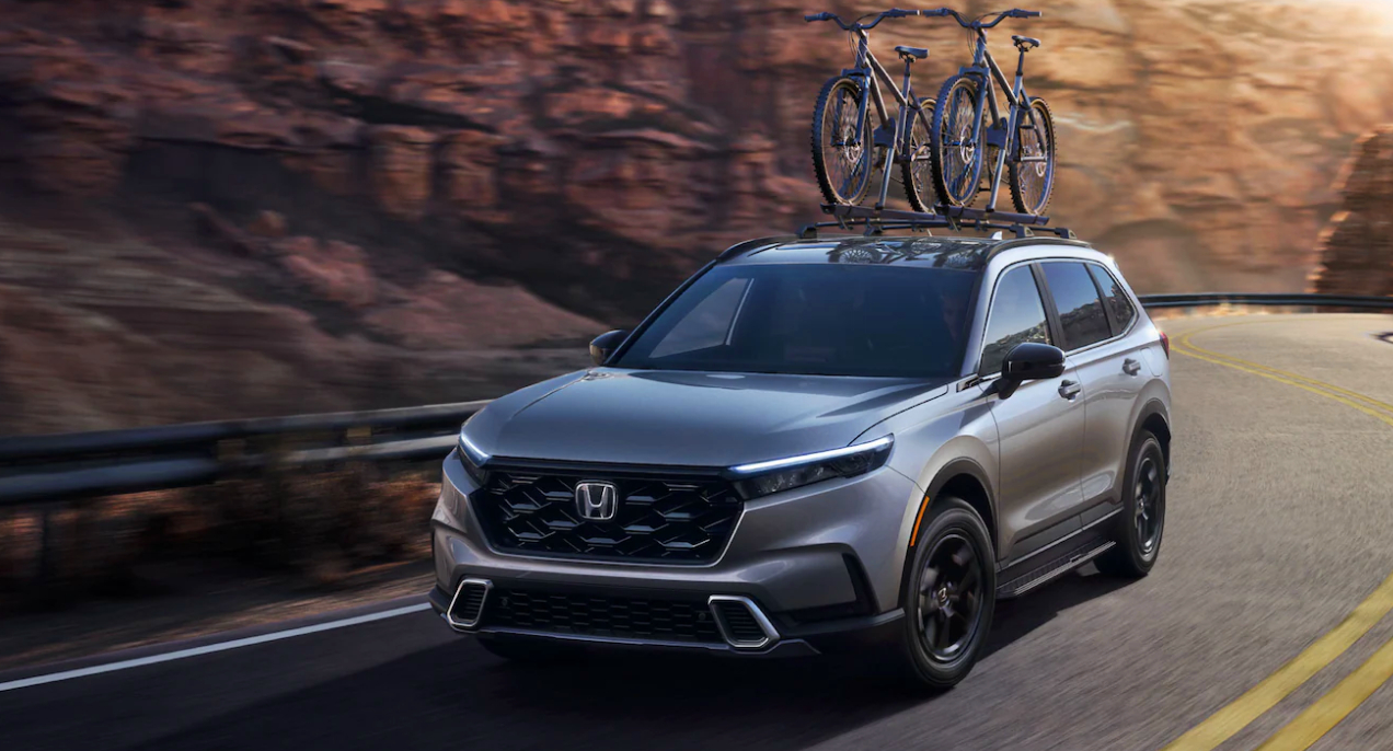 A gray 2023 Honda CR-V small SUV is driving on the road.