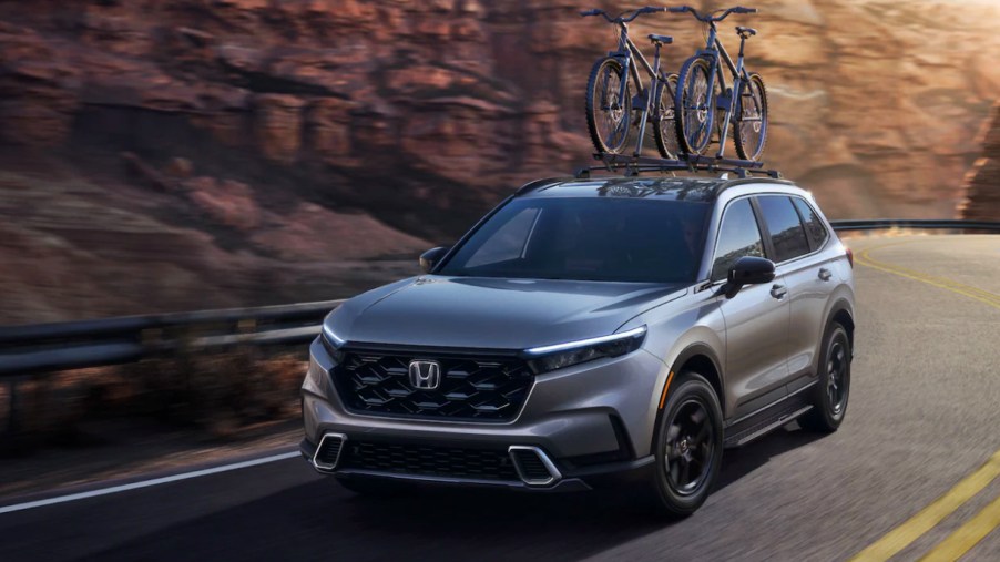 A gray 2023 Honda CR-V small SUV is driving on the road.