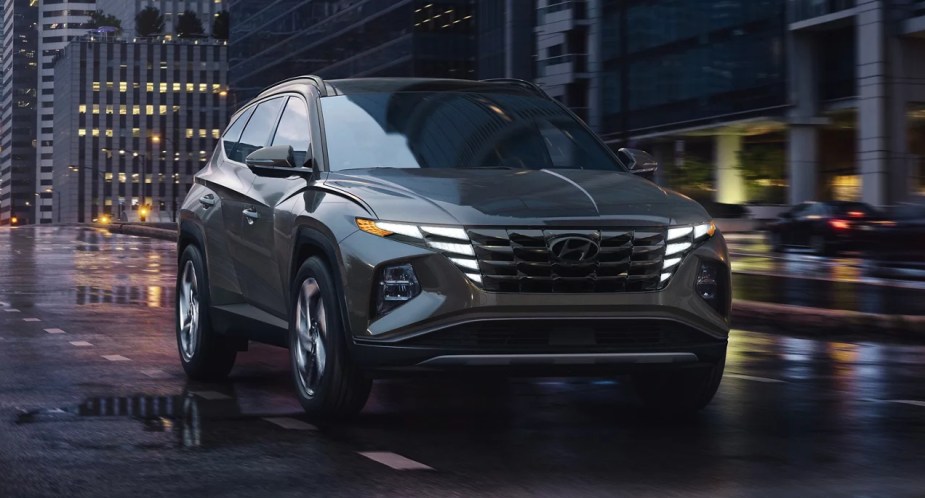 A gray 2023 Hyundai Tucson small SUV is driving on a wet road. 