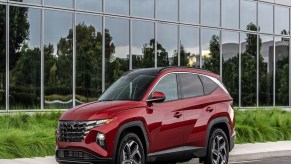 A red 2023 Hyundai Tucson PHEV parked in front of building covered with glass windows.