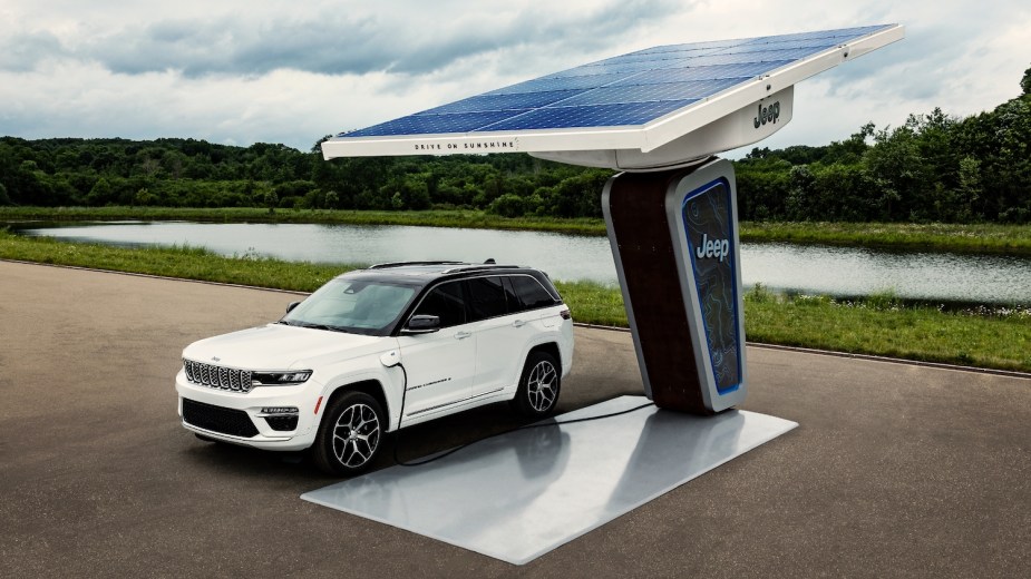 White Jeep 4xe PHEV plug-in hybrid charging its large size battery pack with a solar panel, a river visible in the background