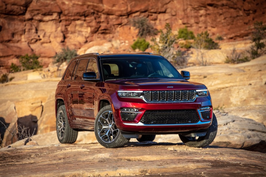 Red Jeep grand cherokee with stock sized tires parked in the desert, a rock outcropping visible behind it.