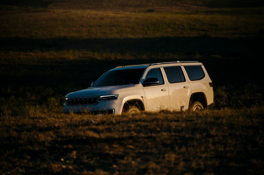 White 2023 Grand Wagoneer SUV driving through a field at sunset, grass visible in the background.