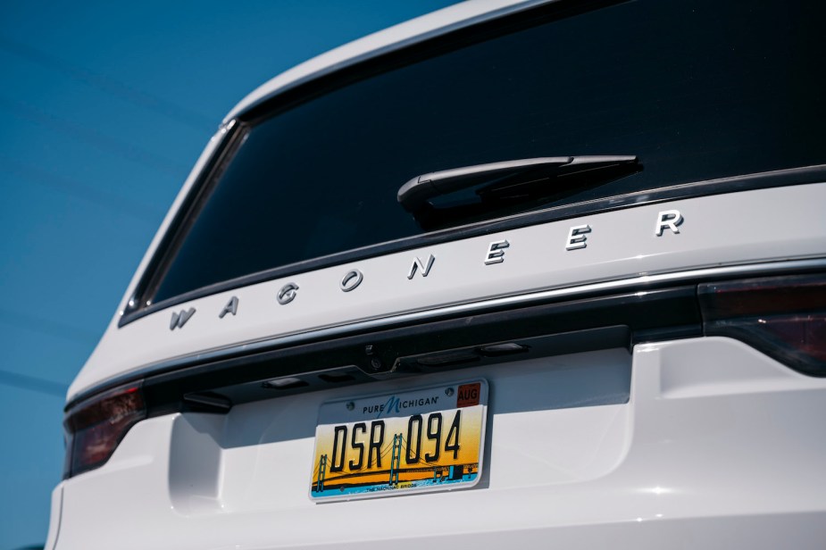 Closeup of the Wagoneer logo on the back hatch of a white 2023 Grand Wagoneer L SUV, the sky visible in the backgorund.