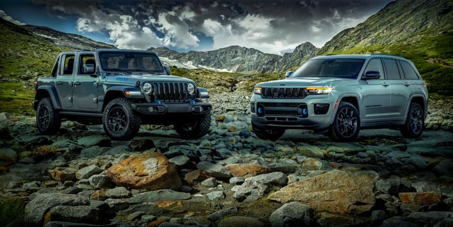 2023 Jeep Wrangler 4xe and 2023 Jeep Grand Cherokee 4xe models parked on a bank of rocks in the mountains