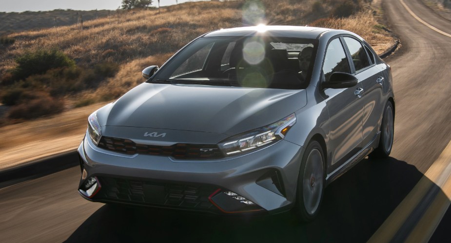 A gray 2023 Kia Forte compact car is driving on the road. 