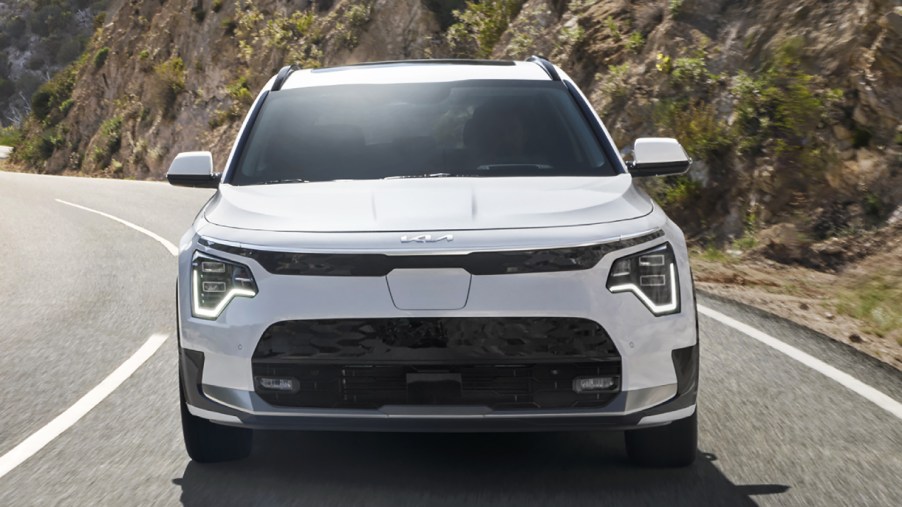 A white 2023 Kia Niro EV subcompact electric vehicle is driving on the road.
