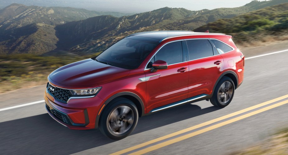 A red 2023 Kia Sorento Hybrid midsize hybrid SUV is driving on the road. 