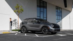A dark gray 2023 Kia Sportage plug-in hybrid electric vehicle (PHEV) compact SUV plugged into a charging station