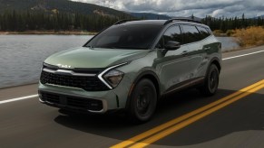 A green 2023 Kia Sportage small crossover is driving on the road.